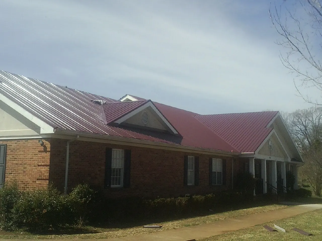 Red metal roof with gabled entries on a long brick building, from a Hail Damage Roof Repair job in Traphill