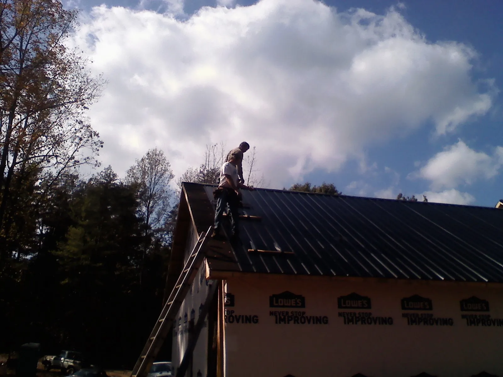 Roofer fastening dark metal panels high against a cloudy sky, from a Roof Inspection job in Traphill